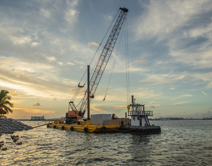 tug boat prepares to pull crane barge to the next job in the setting sun