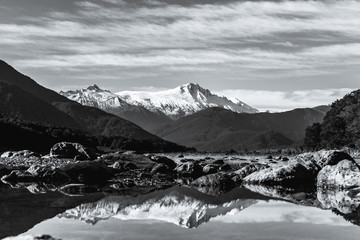 Black and white photo. Stunning landscpae of the reflection of the snow mountain on the river. Blue sky and some cloudy.