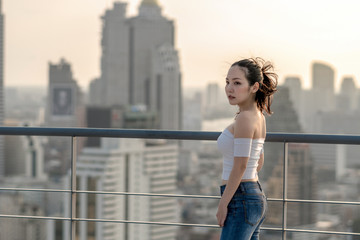 Fototapeta na wymiar Portrait of Asian Yong woman in sexy fashion suit standing on the rooftop over the cityscape background, beautiful shape of body concept