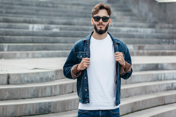 A stylish man with a beard cleans his glasses with a T-shirt. Street photo