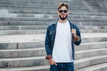 A stylish man with a beard cleans his glasses with a T-shirt. Street photo