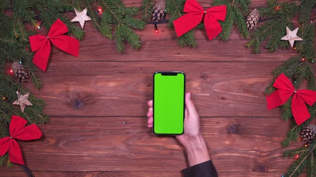 Hand holding phone with green screen on wooden Christmas background