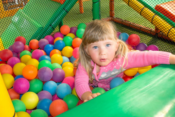 Fototapeta na wymiar Girl playing and having a good time in a ball room on the playground. Happy playing and having fun at kindergarten with colorful balls, family weekend concept. Colorful ball bath for children.