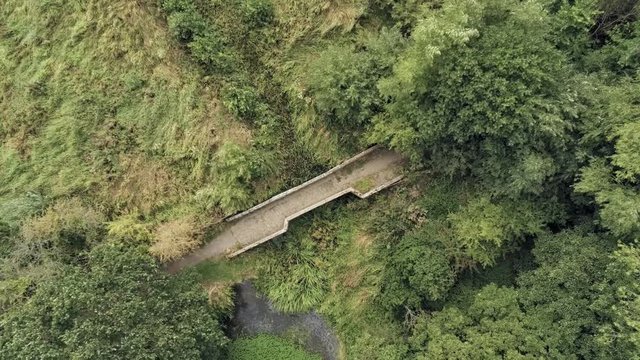 Aerial view, down move. Old small sandstone roman bridge and grass, overgrown water pond in english countryside.