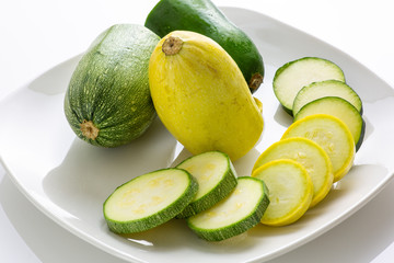 Sliced yellow and green zucchini's on a white plate sitting on a kitchen table waiting to be consumed. 