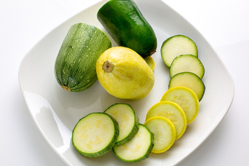 Sliced yellow and green zucchini's on a white plate sitting on a kitchen table waiting to be consumed. 