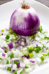 Half a large bulb of sweet onions surrounded by an assortment of chopped onions on a white plate on the kitchen counter waiting for the chef to use them