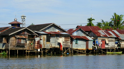 Fototapeta premium einfache Hütten stehen auf Pfählen im Fluss Martapura und spiegeln sich im Wasser