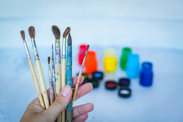 Close up view of female hand with set of paint brushes on blue blurred background with paints cans