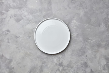 Decorative ceramic empty white handmade plate presented on a gray concrete background with copy space for your menu. Flat lay