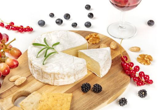 A photo of Camembert cheese with a glass of red wine, fruits and nuts, shot on a white background with copy space