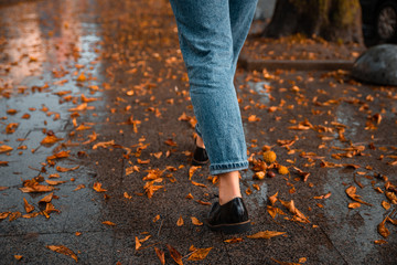 woman walking by wet streets after rain. yellow leaves on ground.