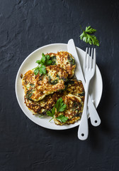 Spinach courgettes fritters - delicious vegetarian snacks, appetizers, breakfast on a dark background, top view