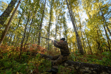 Hunter with a gun in the autumn forest against a background of trees with yellow foliage
