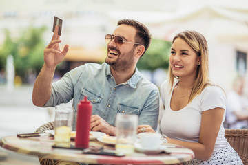 Pay the bill. Attractive young couple holding credit card while siting in sidewalk cafe