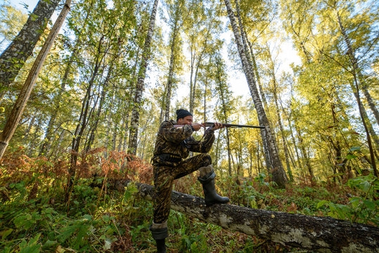 Hunter with a gun in the autumn forest against a background of trees with yellow foliage