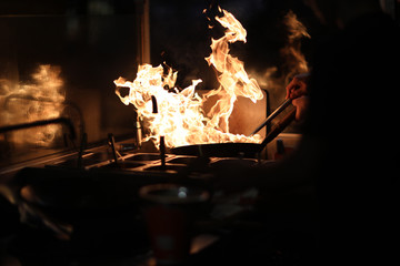 The cook in the kitchen holds a frying pan wok with an open flame and tries to extinguish it with water