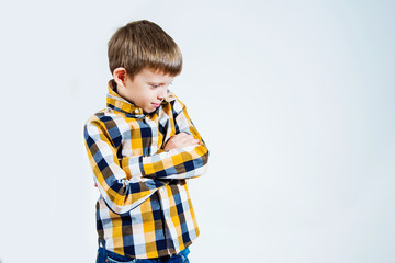 Little boy in a checked shirt on a white background folded his arms and smiles.