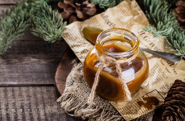 Obraz na płótnie Canvas Homemade salted caramel sauce for christmas dessert in jar on rustic wooden table background. Copy space.