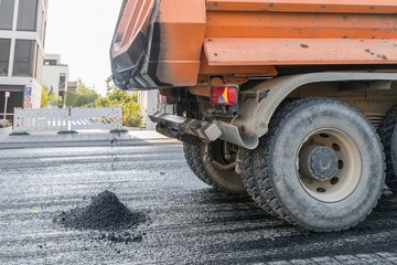 Ein Kipplaster bringt heißen Asphalt für die Erneuerung einer Fahrbahndecke einer Straße,...