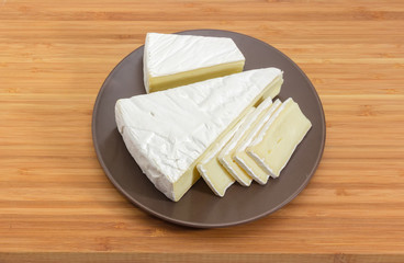 Partly sliced brie cheese on brown dish on wooden surface