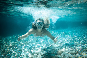 Snorkeling in the tropical sea, woman shows thumb up sign underwater