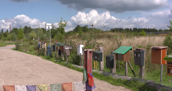 mail boxes lined up alongside a dirt road in countryside. Train of Dutch railways in background.