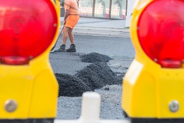 Straßenarbeiter verteilen den heißen Asphalt mit der Schaufel auf der Straße, Deutschland