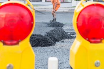 Straßenarbeiter verteilen den heißen Asphalt mit der Schaufel auf der Straße, Deutschland