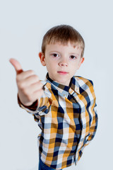 Little boy in plaid shirt on white background shows thumb up with hand and rejoices. Concept - everything is cool.