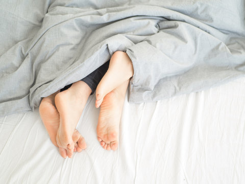 The legs from under the blanket. Young happy couple in bed at home.