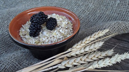Flakes of five cereals in a Cup and fresh blackberries on a wooden background.