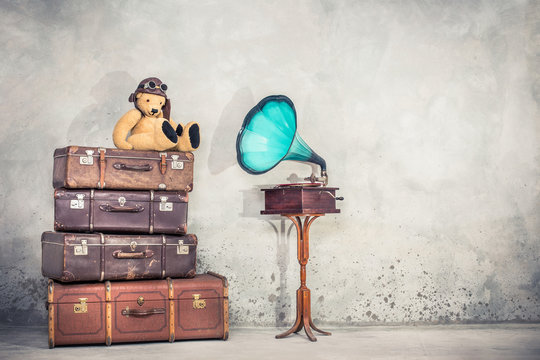 Teddy Bear toy with leather aviator's hat and goggles sitting on retro old aged classic travel suitcases and aged phonograph turntable. Listening music concept. Vintage instagram style filtered photo