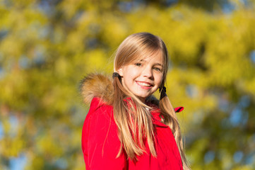 Naklejka premium Fall fashion. Girl smiling face cute hairstyle fashionable fall coat with hood and fur. Kid girl wear coat for fall season. Child cheerful walking wearing warm bright coat or jacket fall sunny day