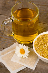 chamomile hot tea with teabags and flowers on rustic wooden table, vertical closeup shot
