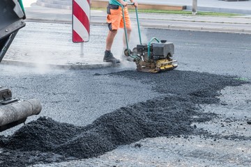 Straßenarbeiter verdichten den Asphalt mit einem Vibrationsstampfer auf der Straße, Deutschland