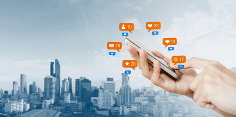 Hand holding mobile smart phone, with notification icons and city background