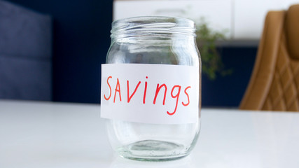 Closeup image of empty glass jar labeled savings on white table