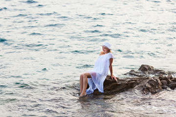 Charming young lady in a white dress among the sea rocks
