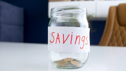 Closeup image of glass jar for money savings with few coins on white wooden desk