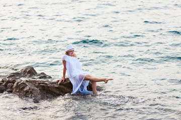 Young blonde splashing water on the rocks in the sea