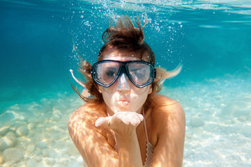 Woman underwater snorkeling in the clear tropical water and blowing a kiss - obrazy, fototapety, plakaty