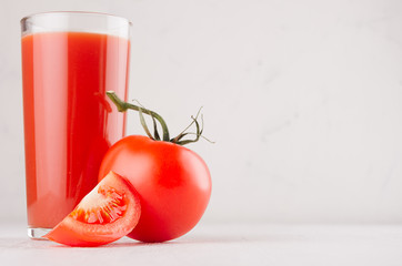 Bright red tomato juice in elegance glass with glossy tomato and ripe piece closeup on white wooden...