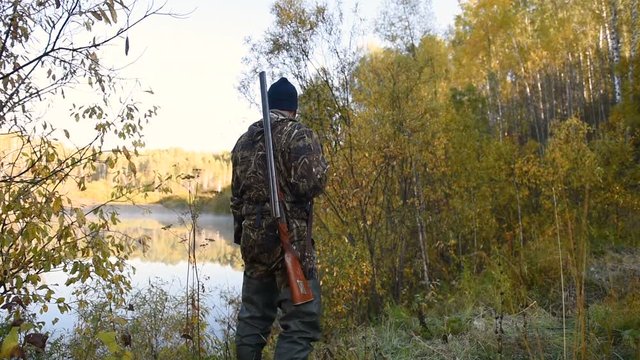 Hunter with a gun goes in the autumn morning by the lake