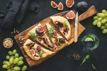 Flatbread with figs, prosciutto, grapes, arugula on wooden serving board. Top view, toned image....