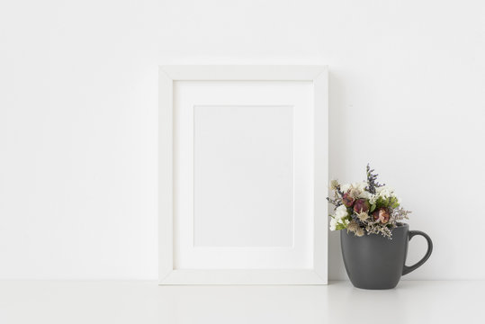 Elegant white A5 portrait frame mockup with small bouquet of dried flowers in a mug on white wall background. Empty frame, poster mock up for presentation design.