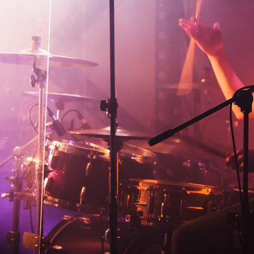 Hand with drumsticks near rock drum set
