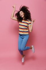 Full length photo of caucasian woman 20s with curly hair having fun and jumping, isolated over pink background