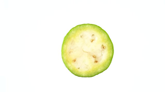 Top view from above of feijoa fruit cross section. One half is slowly rotating on the turntable isolated on the white background. Close-up. Macro.