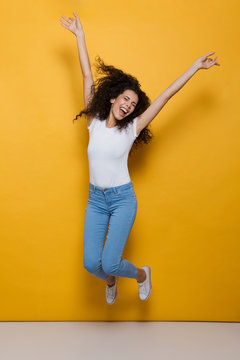 Full length photo of joyful woman 20s with curly hair having fun and jumping, isolated over yellow background